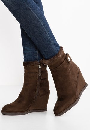 Bottines compensées en daim marron avec zip latéral et bordure en fausse fourrure portées avec un jean skinny bleu foncé.
