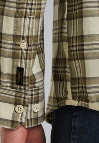 Geruite shirt in beige en olijf groen, met een knoopmanchet en een klein zwart label. Zacht, getextureerd materiaal.