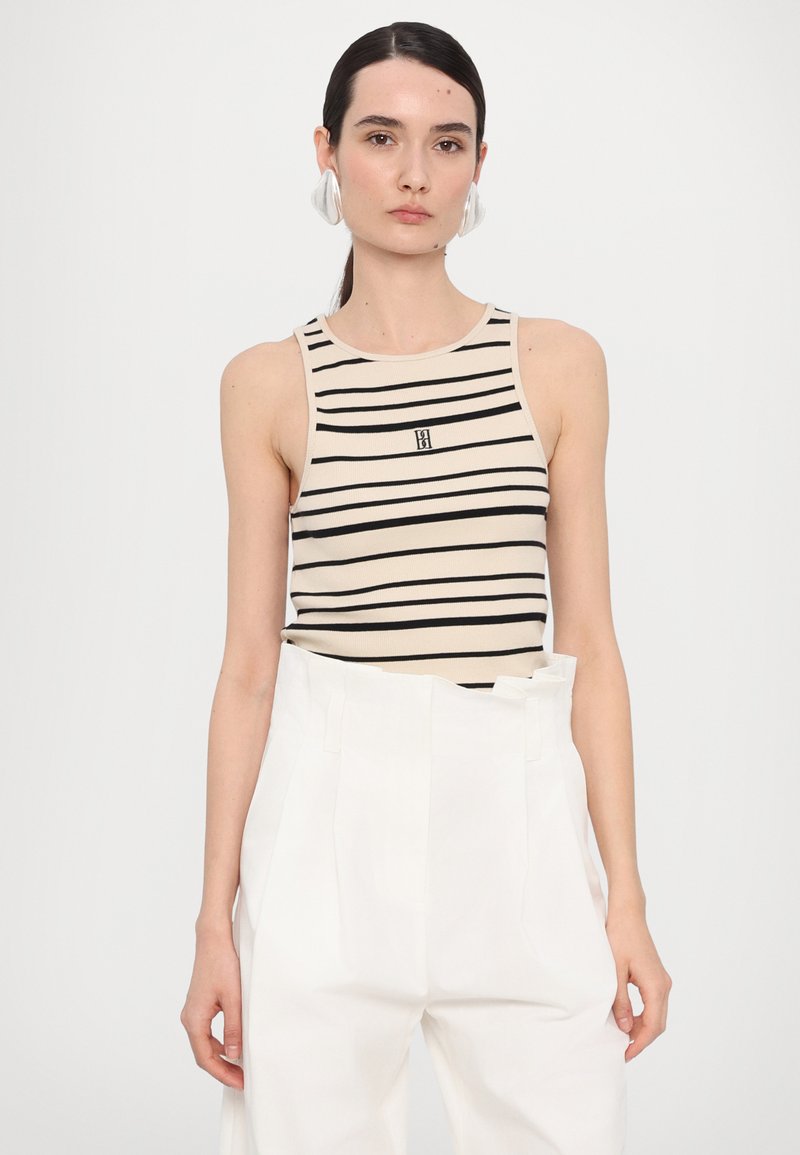 Beige tank top with black stripes, featuring a small logo on the chest. Paired with white high-waisted pants, smooth texture.
