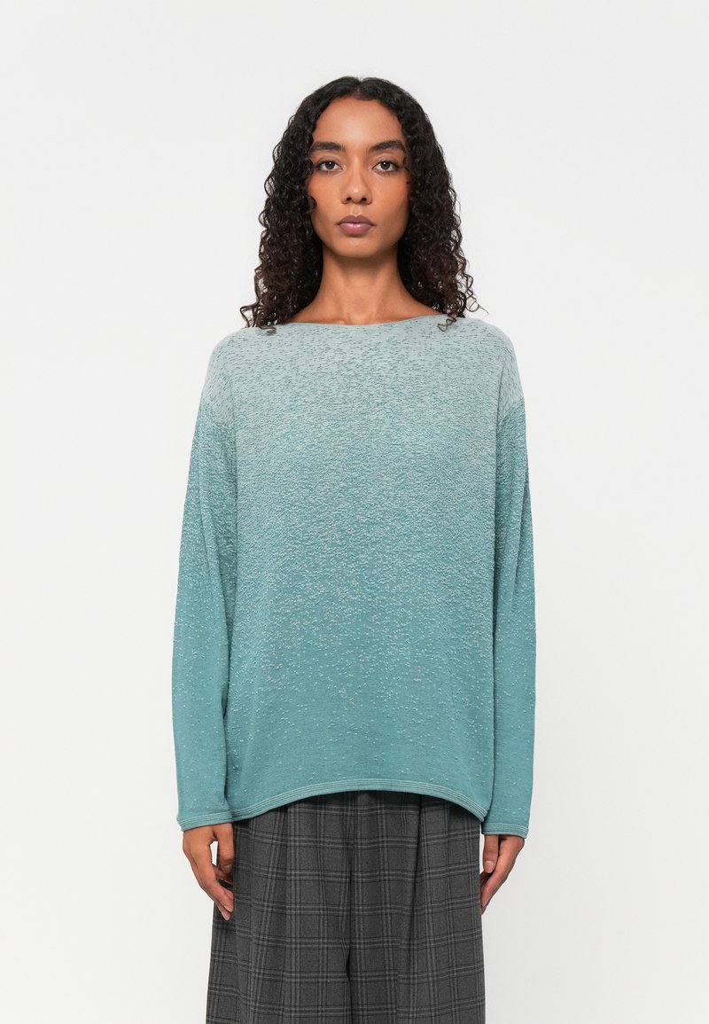 Hellblaues Ombre-Pullover mit strukturiertem Material, weitem Rundhalsausschnitt und langen Ärmeln, kombiniert mit grauen karierter Hose.
