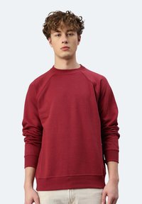 Felpa rossa in cotone con maniche lunghe, scollo tondo e polsini a coste. Presenta una finitura testurizzata e una vestibilità comoda.