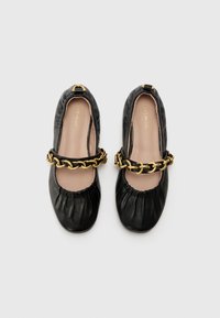 Black leather ballet flats with a gathered toe, gold chain accent across the instep, and a smooth beige interior lining.