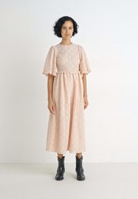 Vestido rosa claro a la altura de la rodilla con patrones en forma de diamante texturizados, mangas cortas acampanadas y una cintura definida. Combinado con botas negras hasta el tobillo.