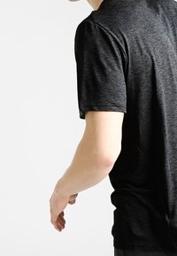 Czarny krótki t-shirt z krótkim rękawem, wykonany z miękkiego, teksturowanego materiału z melanżowym wzorem. Koszulka ma luźny krój i okrągły dekolt.