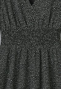 Robe noire avec un décolleté en V, taille smockée élastique, ornée d'un motif à pois blancs et bleu clair. Texture douce, design fluide.