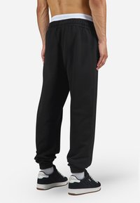 Black sweatpants with an elastic waistband and ribbed cuffs. Soft texture, casual design, pairing with black and white sneakers.