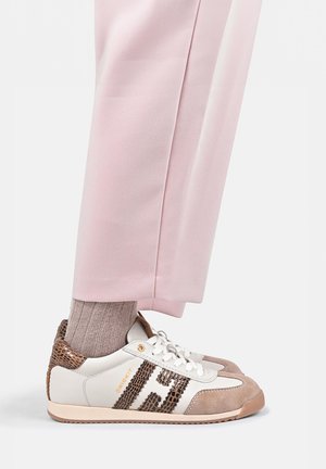 Witte sneakers met bruin suède en slangenhuidpatroon, gedragen met lichtroze broek en beige geribbelde sokken.