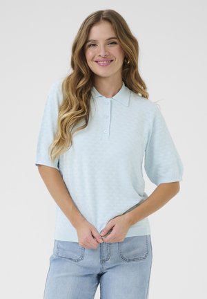 Lichtblauwe polo trui met een gestructureerd ruitpatroon, korte mouwen en een drieknoopsluiting. Gecombineerd met lichte spijkerbroeken.