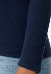 Granatowy sweter dzianinowy o miękkiej teksturze, z długimi rękawami i prążkowanym kołnierzem. Tkanina prezentuje delikatny wzór dzianiny.