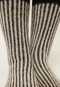 Knit socks featuring vertical stripes in black and cream. Made of textured yarn with a soft, fuzzy appearance and contrasting ribbed cuff.