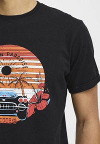 Sort bomulds T-shirt med et farverigt grafisk tryk af en vintage bil, sol, palmer og blomster i orange, blå og røde nuancer.