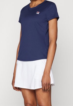 Marineblaues Sport-T-Shirt mit kurzen Ärmeln und Rundhalsausschnitt, mit einem kleinen roten und weißen Logo. Trägt einen weißen perforierten Rock.