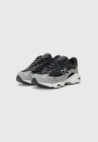 Baskets en cuir noir et gris, avec une tige en mesh, des lacets noirs et une semelle épaisse blanche avec des accents noirs et des détails de marque.