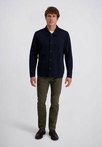 Marinefarbendes Hemd mit Kragen und Brusttasche, kombiniert mit grüner Hose und dunklen Schuhen. Glatter Stoff, lockere Passform.