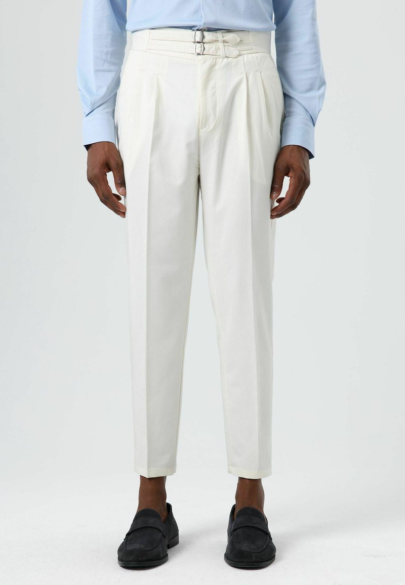 White pleated trousers with double buckle closure, tapered legs, and a smooth texture. Paired with dark slip-on shoes.