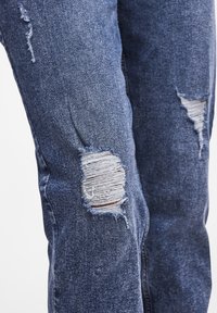 Jeans in denim di colore blu scuro con strappi strappati sulle ginocchia e un leggero sbiadimento. Realizzati in un tessuto morbido e testurizzato con una vestibilità standard.