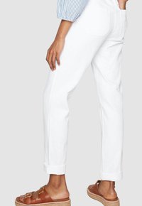 Persona che indossa jeans bianchi con risvolti, una maglietta a righe blu e sandali marroni con doppia fibbia, mostrata dalla vita ai piedi.