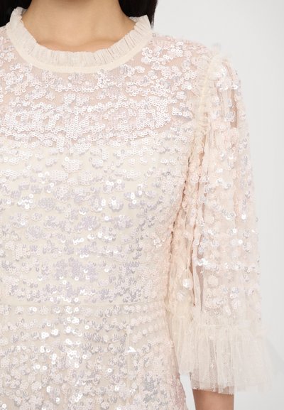 Pärlprydd blus i mjuk beige, med en volangkrage och genomskinliga, texturerade ärmar med frilldetalj.