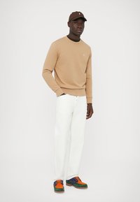 Bēšs džemperis, balti bikses un daudzkrāsainas kurpes. Džemperim ir apļveida kakla izgriezums un logotips. Cepure atbilst džempera krāsai.