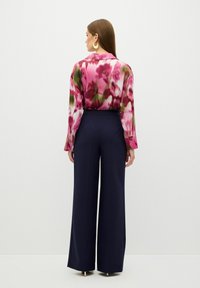 Långärmad blus i blomstertryck i rosa och gröna färger, matchad med midjeförhöjda byxor med vida ben i marinblått. Guldörhängen i form av ringar synliga.