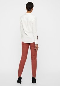 White long-sleeve shirt with a back yoke detail, paired with fitted rust-colored pants and black high-heeled shoes. Minimalist design.