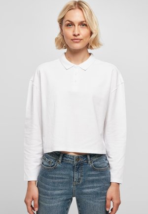 Hvid cropped langærmet polo shirt med krave og tre-knaps placket, parret med blå denim jeans med forlommer.