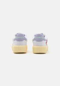Baskets blanches avec des accents lilas pastel et des éléments en vert. Présentent une semelle en caoutchouc beige texturée et un onglet au talon avec marque. Design simple et moderne.