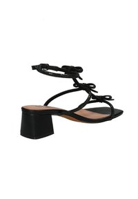 I sandali neri con tacco alto presentano un tacco spesso e un design sottile con cinturini e fiocchi. Il materiale è liscio con una finitura opaca.