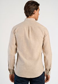 Beige shirt met lange mouwen en een subtiele textuur, voorzien van een plooitje aan de achterkant, manchetten met knopen en een afgeronde zoom.
