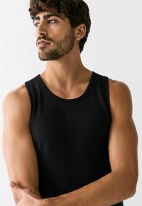 Canotta nera a costine, design senza maniche, scollatura tonda classica, modello aderente, realizzata in materiale morbido, indossata da un modello maschile.