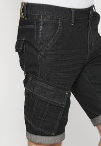 Melna denim drēbju bikses ar klasisku griezumu, vairākiem kabatām un kontrastu šuvēm. Ritināta apakšmali un teksturēts audums izturībai.