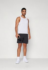 Men's athletic outfit featuring a white sleeveless top and black shorts. Notable details include a small logo on the shorts and a handheld water bottle.