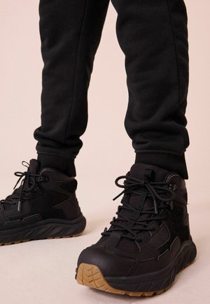 Sorte høj-top sneakers med tekstureret stof og gummidetaljer. Har robuste snørebånd, en polstret sål og en kontrasterende gummisål.