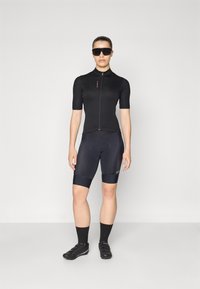 Svart sykkeltrøye med korte ermer og glidelås, kombinert med svarte sykkelshortser. Brukt med svarte solbriller og sykkelsko.
