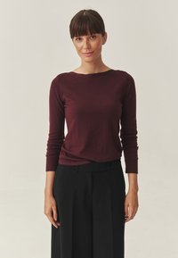 Burgunderfarbener Longsleeve-Oberteil aus weichem Stoff, mit Rundhalsausschnitt und taillierter Silhouette, kombiniert mit maßgeschneiderten schwarzen Hosen.