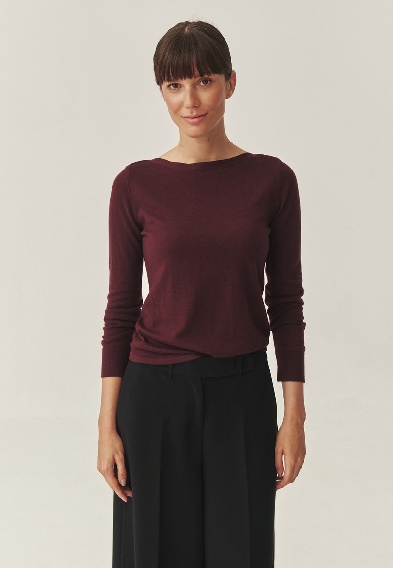 Burgunderfarbener Longsleeve-Oberteil aus weichem Stoff, mit Rundhalsausschnitt und taillierter Silhouette, kombiniert mit maßgeschneiderten schwarzen Hosen.