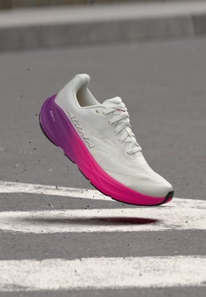 Zapatilla de correr blanca y rosa con cordones, de la marca Altra, en el aire sobre asfalto con marcas viales blancas.