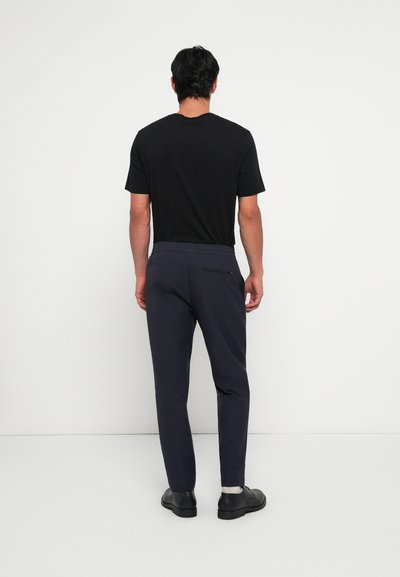 Camiseta negra y pantalones azul marino con cinturilla elástica y un bolsillo trasero. Los pantalones tienen un corte ajustado y están hechos de una tela suave.