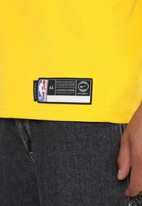 Žlutá NBA dres swingman s označením NikeConnect, velikost 44, nošený s černými džíny a viditelnou pravou rukou.