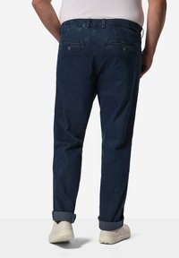 Tmavě modré denimové kalhoty se rovný fit, s zadními kapsami a ohrnutými manžetami, doplněné světle béžovými teniskami.