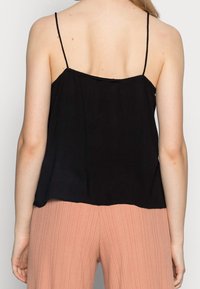 Top nero senza maniche con spalline sottili, caratterizzato da una vestibilità ampia e una texture morbida, abbinato a pantaloni rosa chiaro plissettati.