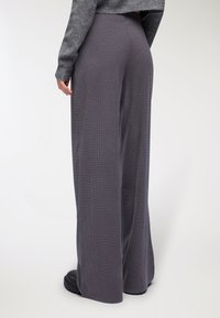 Szerokie spodnie w ciemnoszarym prążkowanym materiale, charakteryzujące się teksturowanym wykończeniem i luźnym krojem. Czarne obuwie widoczne na dole.