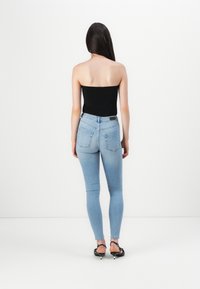 Svart stroppeløs topp, lyseblå skinny jeans og svarte hælede sandaler med sølvdetaljer, sett bakfra mot en ensfarget bakgrunn.