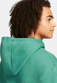 Turkosa hoodie med mjuk textur, med en rymlig huva och sömdetaljer. Tyget verkar tjockt och hållbart, designat för avslappnad användning.