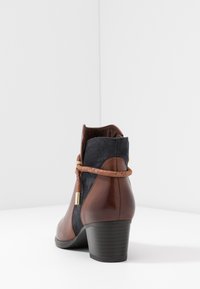 Bottine en cuir marron et daim bleu marine avec un petit talon, ornée d'une bride tressée marron et d'un accent doré.