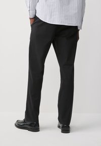 Czarne spodnie o prostym kroju, wykonane z lekkiego materiału, charakteryzujące się gładką fakturą i subtelnymi detalami przeszyć.