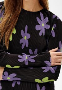 Długi rękaw top w czarnej, prążkowanej tkaninie z fioletowymi i zielonymi wzorami kwiatowymi. Posiada okrągły dekolt oraz dopasowany krój.