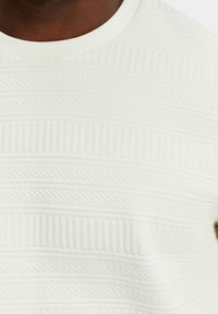 Vit texturerad skjorta med horisontella linjer och zickzackmönster, rund halsringning och mjukt, mönstrat tyg.