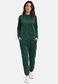 Groene sweatshirt en bijpassende joggers van zachte stof, met een ronde hals, ribgebreide mouwen en elastische manchetten, gecombineerd met witte sneakers.
