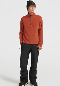 Orange fleecepolo med halvdragkedja, matchat med svarta byxor. Inkluderar en svart mössa och bruna vinterskor.